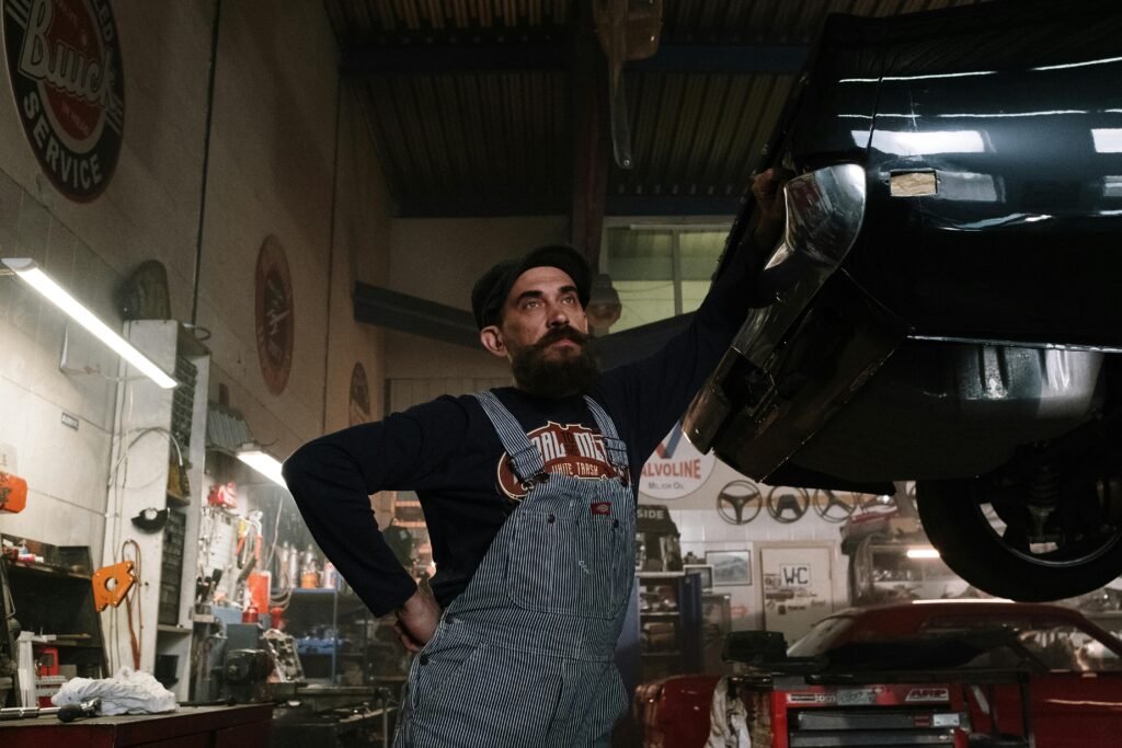 Bearded mechanic working under a classic car in a vintage garage setting. Perfect for automotive themes.